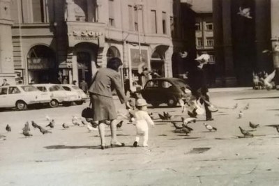 A Woman and Child Feeding Pigeons on Liberty Square, Small Cars at the Kerb, Novi Sad, 1960s
